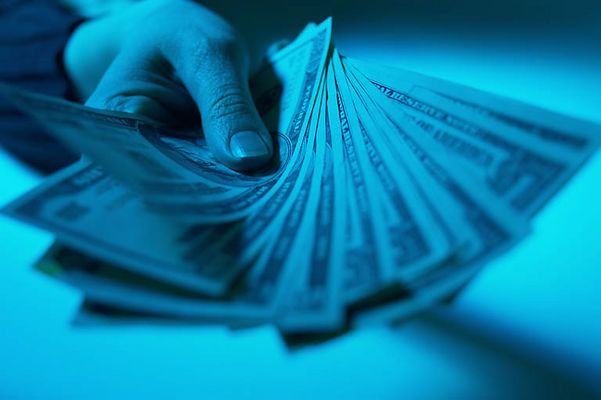 Caucasian man holding spread of American bills in blue light.jpg
