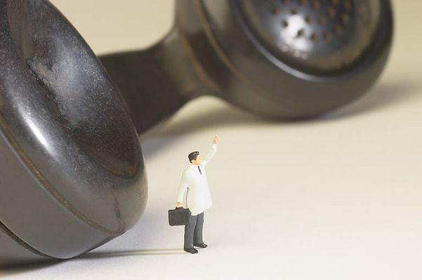 Miniature businessman standing beside black plastic phone receiv.jpg