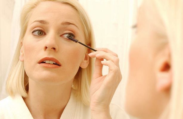Woman putting on mascara in bathroom mirror.jpg