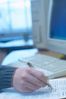 Caucasian man hand writing report on desk with pen beside comp.jpg