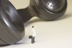Miniature businessman standing beside black plastic phone receiv.jpg